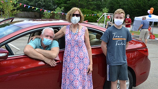 Mother and son wearing masks near their red car