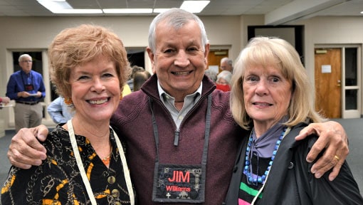 Three senior adults smiling together in a hallway