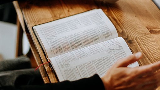A bible on a wooden table next to a cup of coffee