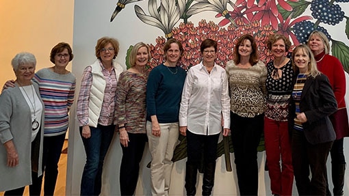 A group of women smiling against a wall with large flower wallpaper
