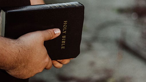 A man's hand holding a black Bible