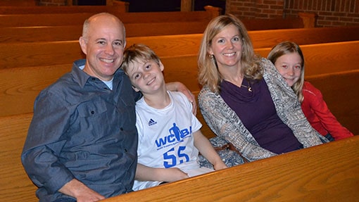 A mom, dad, and two boys sitting a wooden pew together